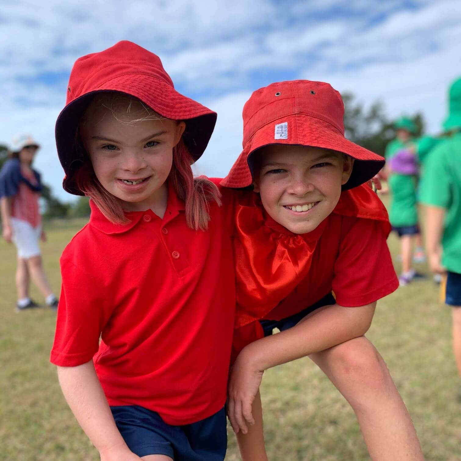 Two students a boy and girl wearing red school uniforms and bucket hats.