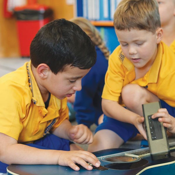 Two young boys play with a guitar