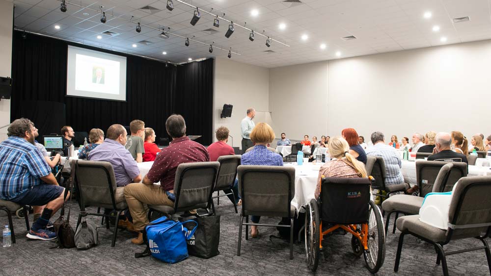 A conference room full of people listening to a speaker