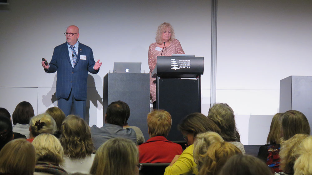 Two people presenting behind a podium to a room of people