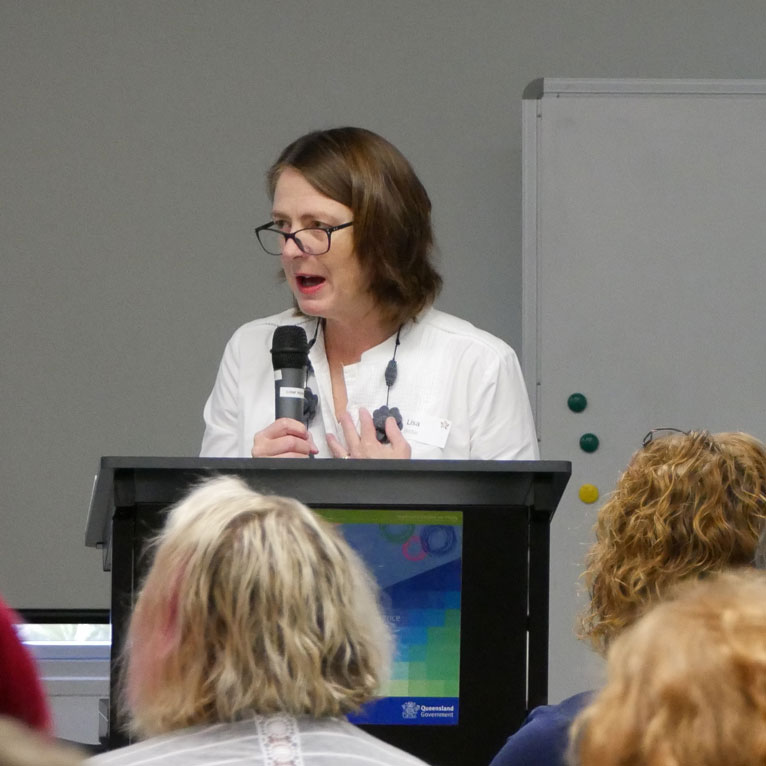 A woman holding a microphone presenting in front of a group of people